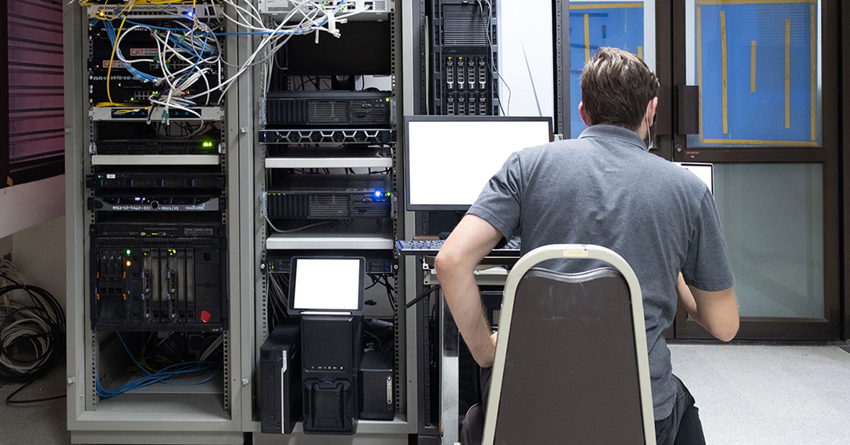 Photograph of on-premises IT specialist seated in front of server cabinets, reviewing his terminal screen.