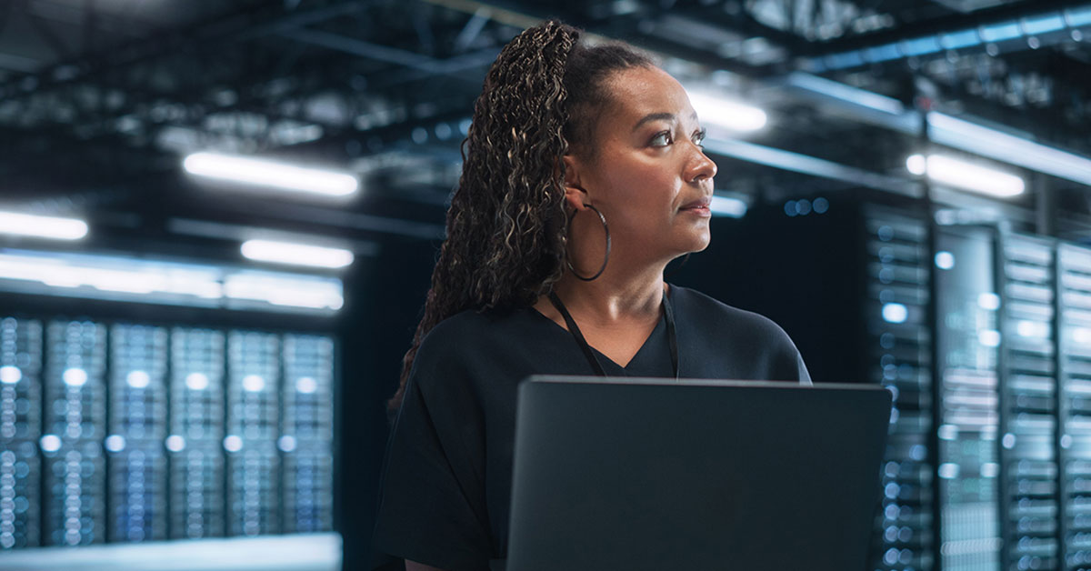 Photograph of data center administrator holding laptop while she walks around storage corridors.