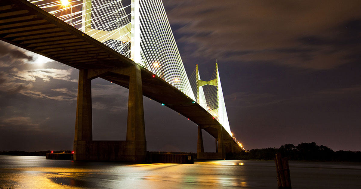 Photograph of a tall, brightly illuminated bridge over a river at night.